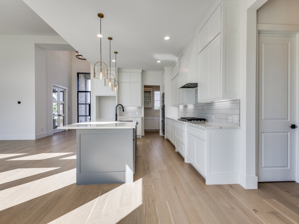 Open custom kitchen with white cabinetry, waterfall island and black fixtures