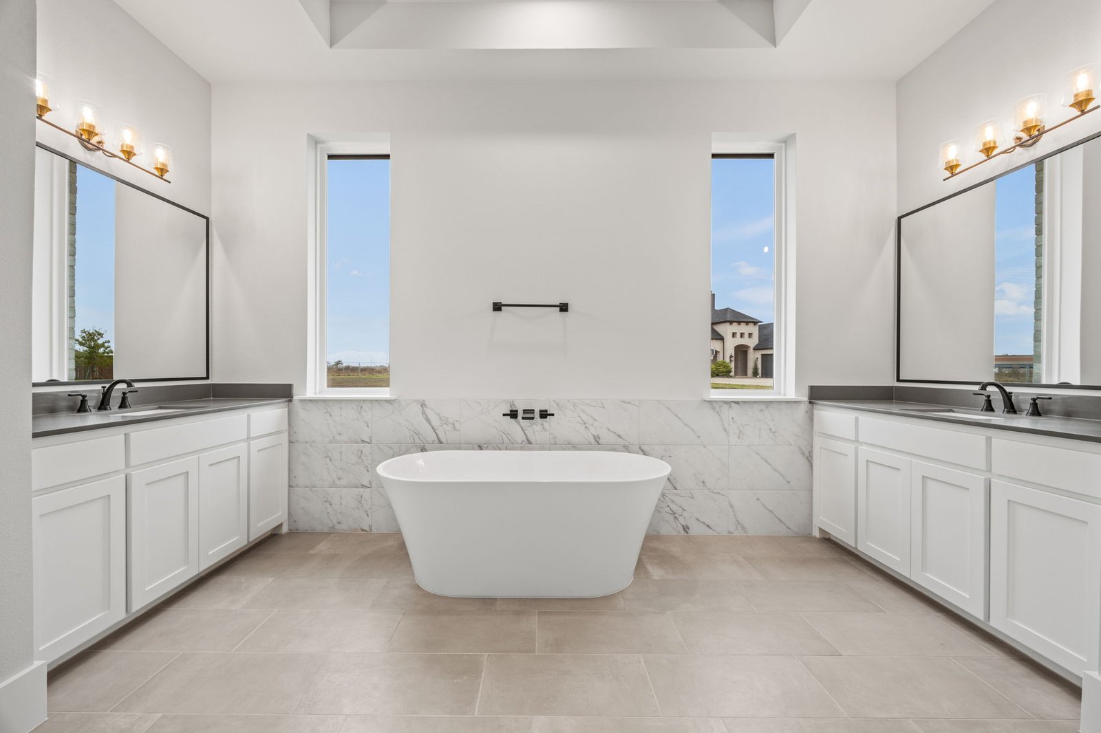 Primary bathroom with a freestanding tub, dual vanities and tall windows