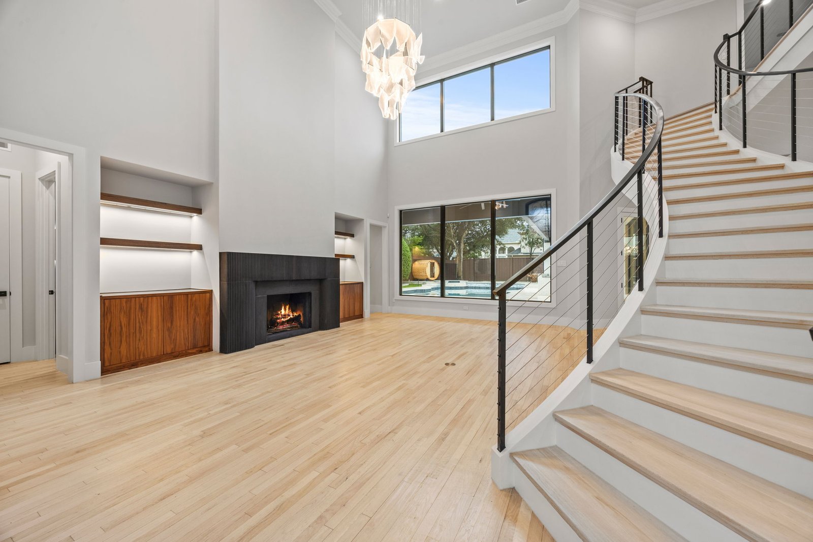 Renovated double-height great room with fireplace, custom built-ins and curved staircase in West Plano