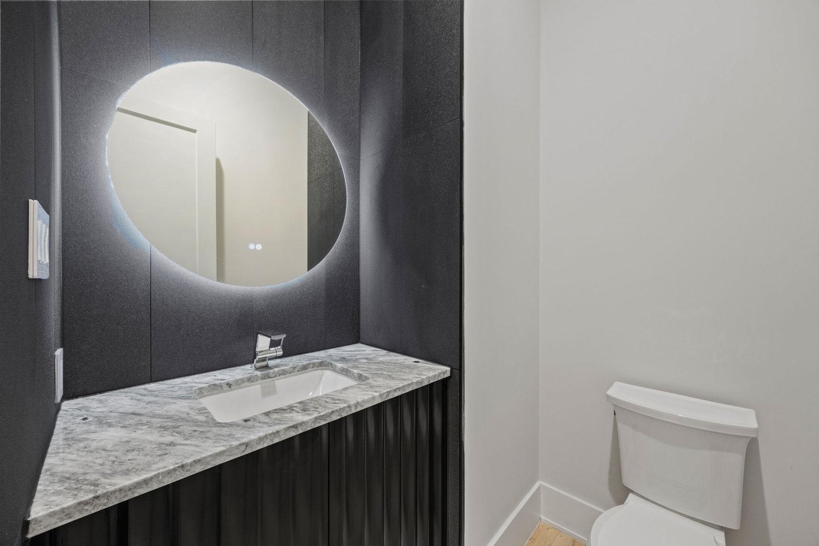 West Plano powder bathroom with dark wall paneling, a backlit round mirror and stone vanity